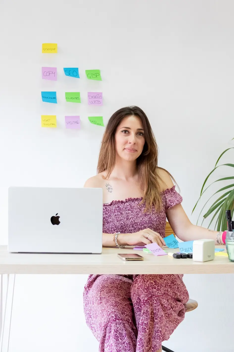 Mujer trabajando con portátil y teléfono, fondo con notas adhesivas de colores. Laura G.Arias.